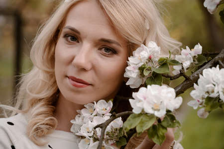 Adult blonde woman portrait enjoying flowering tree in spring gardenの写真素材