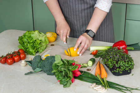 Woman cutting fresh vegetables for salad in kitchenの写真素材