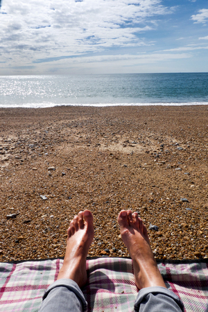 women's bare feet and jeans, personal perspective, pebble beach, sea and sky in sunの写真素材