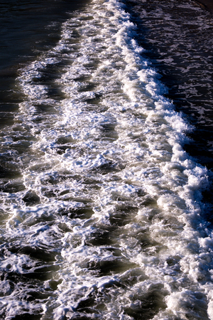 small wave breaking photographed from above, breaking wave running in a line through centre of the image, sea on both sides, white foamの写真素材