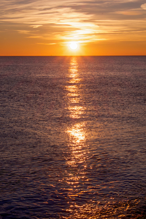 low sunset sun with sunbeam in the centre casting long highlight from the sun accross the sea, the sea is bottom two thirds of photograph and the sunset sky is one third of photographの写真素材