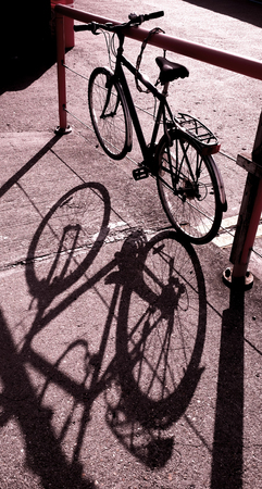 bicycle tied uo in sun light casting strong shadow of bycicle on concrete groundの写真素材