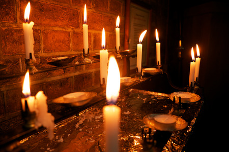 8 burning white candles in a church, the foreground candle is out of focus and the others are in focus,の写真素材