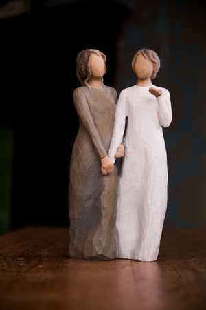 wooden statue 30cm meters high, of two womwn holding hands affectionately, statue is on a wooden surface with a black background, the statue of the women is carved wood, one women is wearin a long green dress and the other a white dress, this staue could の写真素材