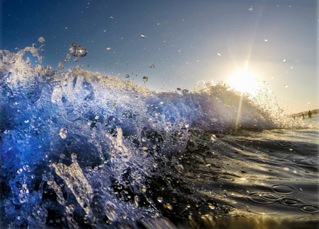 close up in the sea of a Wave breaking, white foam, sun shining behind making water glistenの写真素材