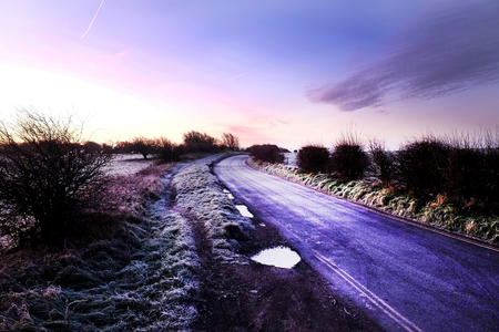 A country lane with a curve to the right, frost on the road and the countryside, red dawn light rising in the skyの写真素材