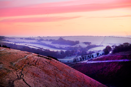 A deep gorge running through the countryside, red dawn light rising in the sky, rolling hills in the background, rolling green hills in the background.の写真素材