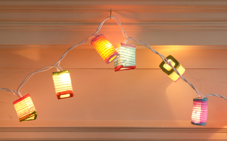 small christmas lantern lights, red, orange, blue green hanging on a mantlepiece in a houの写真素材