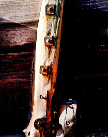 Wooden, weathered sea defence wall, three gnarled planks of wood running horizontally accross the image and a thick vertical wooden post with three big rusty bolts on it, lots of wooden textureの写真素材