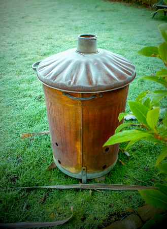 a garden fire bin with frost on it in a garden green grass in the background, graphical style, incinerator, fire incinerator, texture & circular shape, leaves from a plant on the right hand side of the imageの写真素材