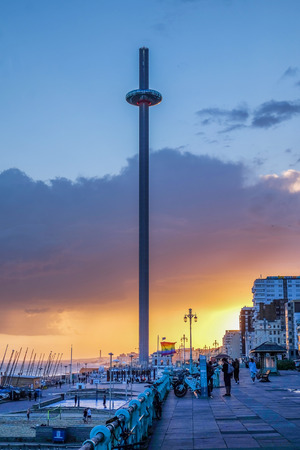 Brighton promenade at sunset with the moving viewing tower in the centre the promenade is very busy a pride flag is flying in the background the sky is orange and red from the setting sunのeditorial素材