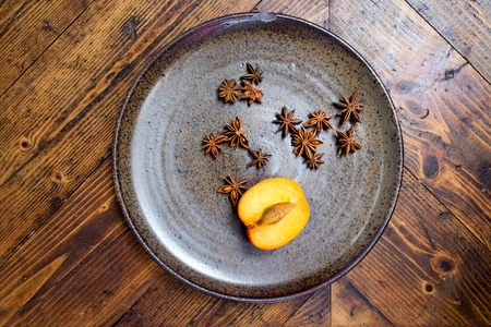 still life photograph of ten star anise and a half of a peach on a rustic stone circular plate on a wooden rustic table topの写真素材