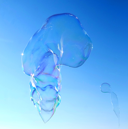 A big bubble floating in the sky, the sky is bright blue behind, the bubble is transparent but is reflecting colours of the spectrum at itâs edgesの写真素材