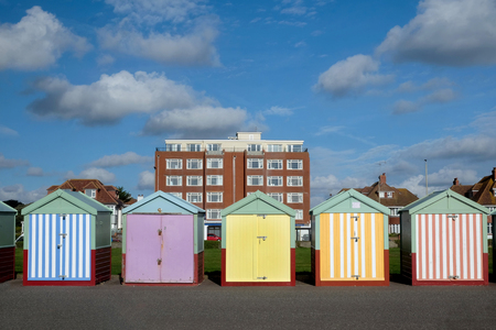 Brighton seafront five beach huts, with multi coloured doors of yellow, pink, black stripes behind is an appartment building and blue skyの写真素材