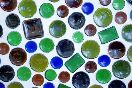 Fifty circular glass bottles have been reused as building materials and the bottom of the bottles are built into a white wall, the bottles have just the bottom of the circular glass showing, they are blue, green and brownの写真素材