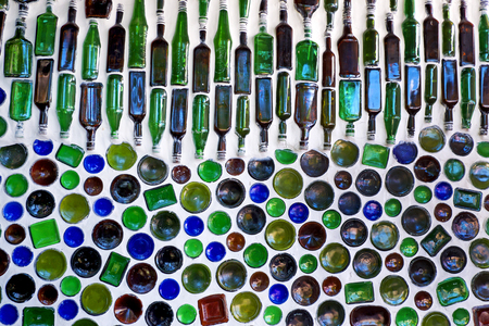 one hundred glass bottles built into a white wall, fifty of the bottles in the bottom of the image have just the bottom of the circular glass showing, the bottles in the top half have are laid on their side and so all of the shape of the bottles can be seen they are blue, green and brownの写真素材