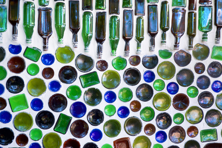 one hundred glass bottles built into a white wall, fifty of the bottles in the bottom of the image have just the bottom of the circular glass showing, the bottles in the top half have are laid on their side and so all of the shape of the bottles can be seen they are blue, green and brownの写真素材