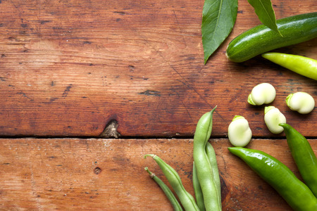 green beans, broad beans clove leaves and green chilli on a rustic wooden table top, the vegetables are arranged on the right side of the image leaving space on the right side of the chopping board for copy space, still life, horizontal formatの写真素材