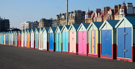A line of twenty five multi coloured beach huts on Brighton promenade with a diminishing perspective, the sun is shining with a blue sky.のeditorial素材
