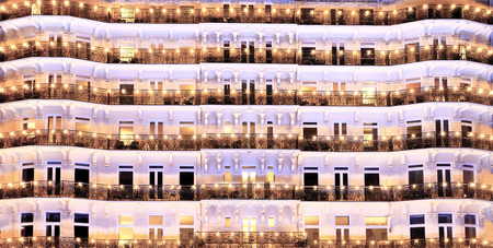 The repeating patterns of the front of a white grand regency hotel pink building with ornate shapes, black ironwork balconies and windows, the balconies are covered in hundreds of orange lightsの写真素材