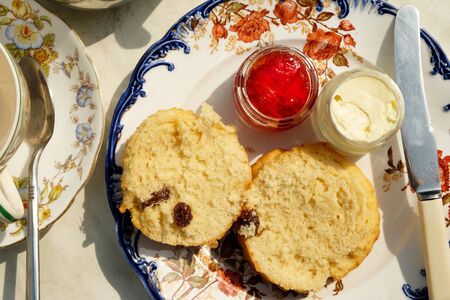 A close up of an english afternoon cream tea on it, a round plate with a scone strawberry jam and cream, an empty cup and saucer for tea and a silver tea pot next to it.の写真素材