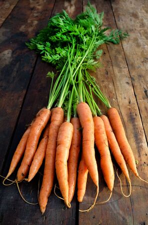 freshly picked organic carrots on a rustic wooden table top, home grown, plant based, above view, vertical formatの写真素材