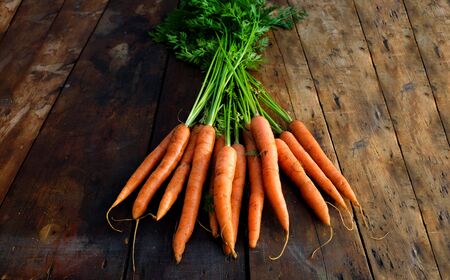 freshly picked organic carrots on a rustic wooden table top, home grown, plant based, above view,の写真素材