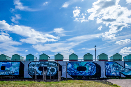 A line of beach huts ontop of a congrete wall with graffiti in the top half of the photo is a big blue and white cloudy dramatic sky, Hove, Brighton, East Sussex, England, United Kingdom, UKのeditorial素材