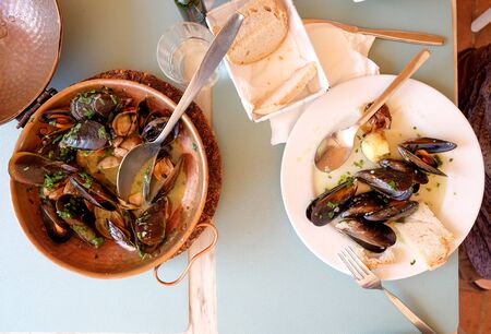 a restaurant table with a copper serving bowl and white plate full of mussels and clams, garlic and parsley a traditional Portuguese dish called Ameijoas a Bulhao, Vilamoura, Algarve, Portugalの写真素材