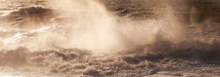 A line of white spray capturing the dramatic moment a wave breaks in a rough stormy sea sending white spray and waves high in to the air, motion and blurの写真素材