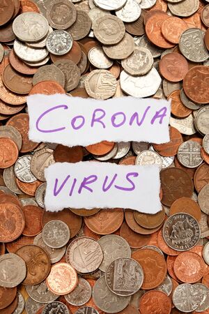 The words corona virus written in purple ink on two pieces of ripped white paper laying on top of hundreds of silver and copper coloured coins, pound sterling British currency, vertical formatの写真素材