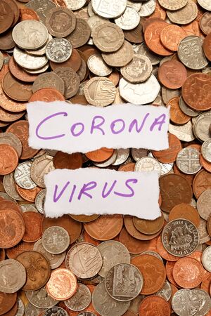 The words corona virus written in purple ink on two pieces of ripped white paper laying on top of hundreds of silver and copper coloured coins, pound sterling British currency, symbolising corona virus crisis and moneyの写真素材