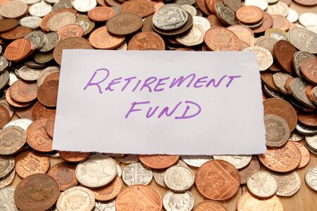 The words retirement fund written in purple pen on white paper, the paper is on top of hundreds of silver and copper coloured British coinsの写真素材