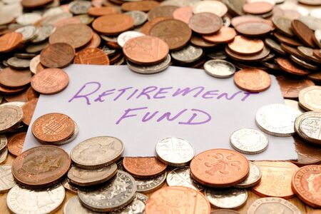 The words retirement fund written in purple pen on white paper, the paper is on top of hundreds of silver and copper coloured British coinsの写真素材