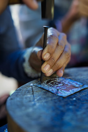 Close up of a hand of a Thai craftsman working on a metal piece on a wooden table