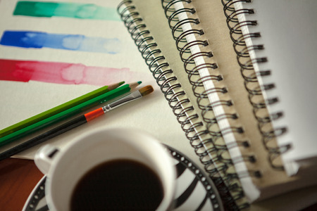 Colored pencils and paintbrush on a wooden desk and colored sketch Abstract background with coffeeの写真素材