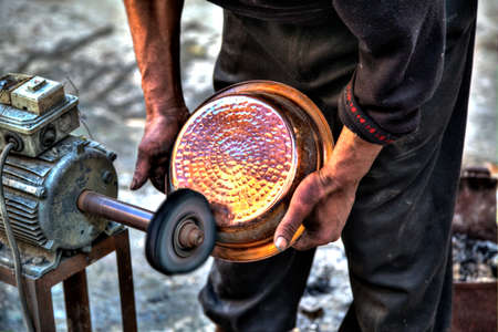 A craftsman in the Kingdom City Fes in Morocco in Africa is polishing at a polishing disk a copper potの写真素材