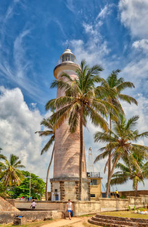The famous lighthouse in the Galle Fortress with a stunning cloudy sky and beautiful old coconut palm trees on the tropical island Sri Lanka in Asia in the Indian Oceanのeditorial素材