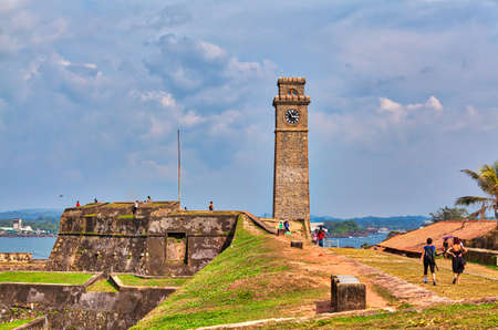 The famous clock tower in the historical Galle Fortress on the tropical island Sri Lanka in Asia in the Indian Ocean with beautiful blue sky and lots of luminous green plantsのeditorial素材