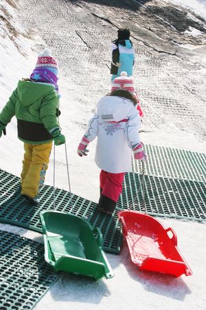Students in colorful ski clothing pull sleds up a hill