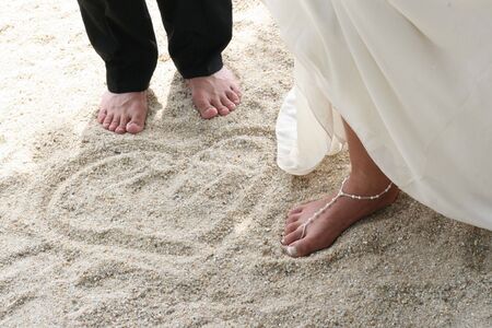 Bride and groom next to a love heart pattern in the sand.の写真素材