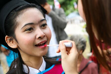 Asian university graduate having her lipstick applied by a make-up artist.の写真素材