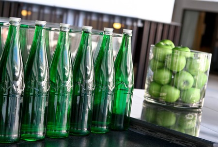 Row of bright green bottles and container of apples on a bar.の写真素材