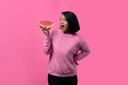 Attractive young Asian woman wearing sweater and holding watermelon pieces