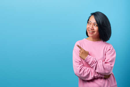 Cheerful Asian woman pointing to empty room on blue backgroundの写真素材
