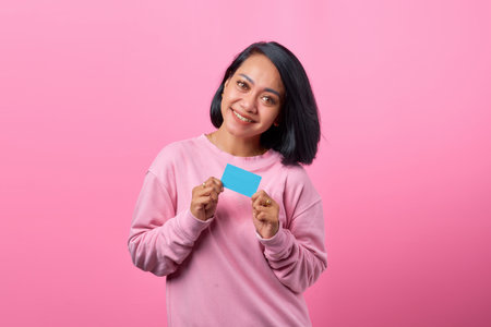 Portrait beautiful young asian woman smile with credit card on pink backgroundの写真素材