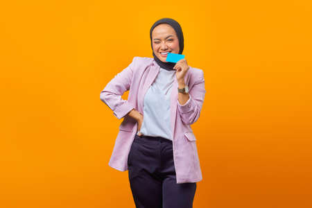 Beautiful Asian woman biting blank card and looking at camera over yellow backgroundの写真素材