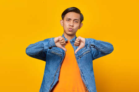 young asian man looking unhappy ang anry showing rejection with thumbs down gesture