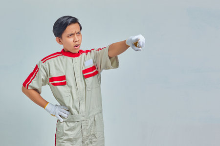 Portrait of surprised handsome man wearing mechanical uniform pointing with open finger and mouth on gray backgroundの写真素材