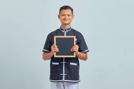 Portrait of excited Asian young man wearing karate uniform showing blank board on gray backgroundの写真素材